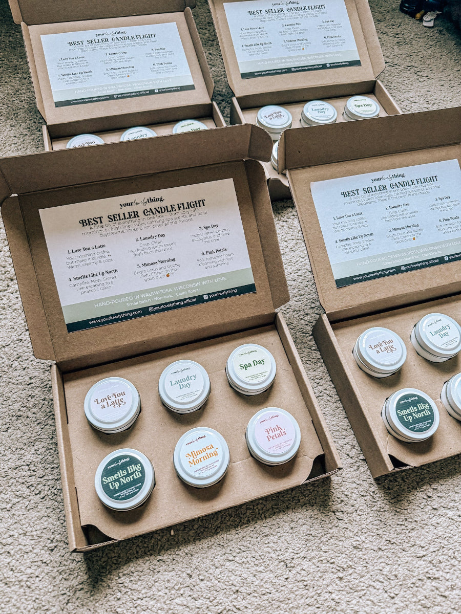 Open cardboard boxes containing small candles with labels on a carpeted floor.