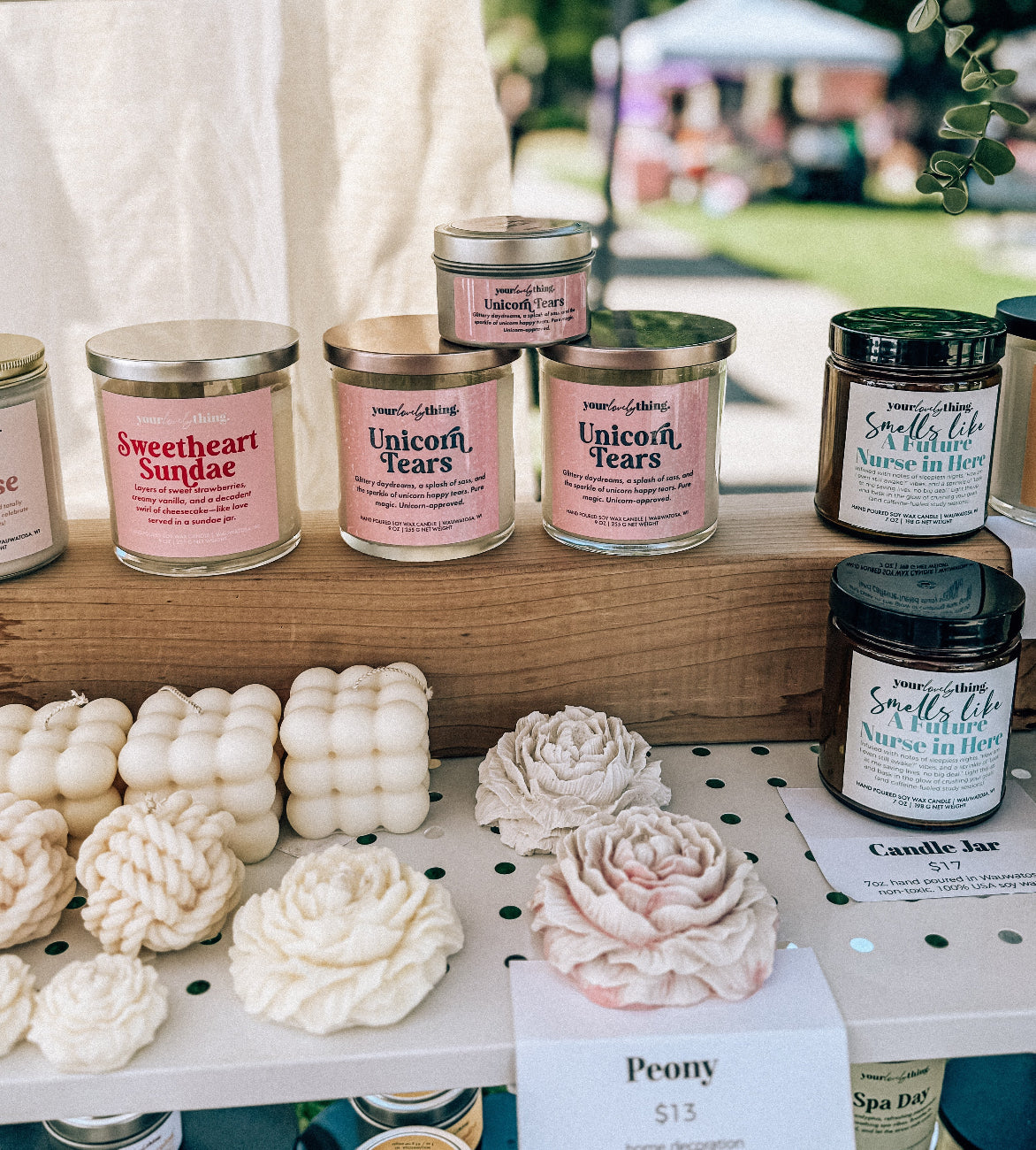 Candles and home decor on display with visible branding at an outdoor event.