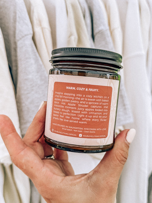 Hand holding a candle jar with a label against a neutral background