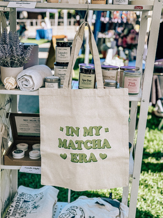 Beige tote bag with 'In my matcha era' text on a display rack with products.