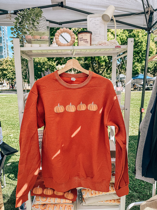Orange sweatshirt with pumpkin design on a hanger outdoors