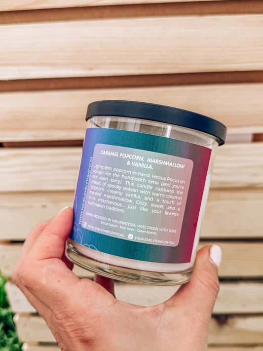 Hand holding a candle jar with a label against a wooden background