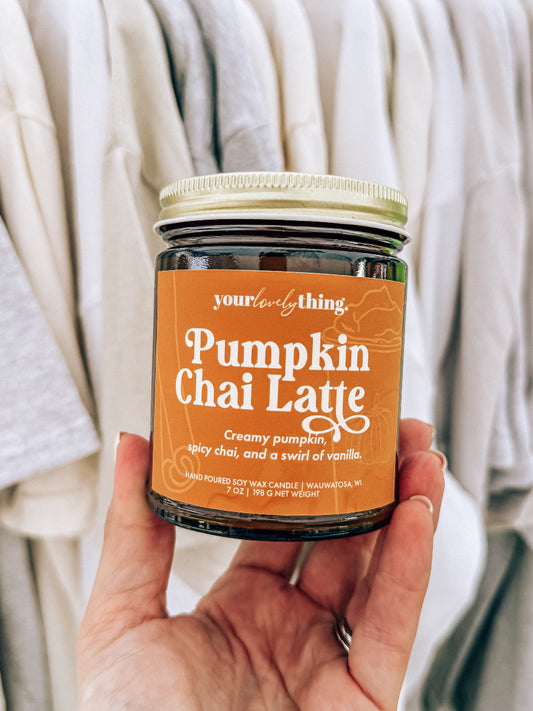 Jar of 'Pumpkin Chai Latte' candle held by a person wearing a light-colored sweater.