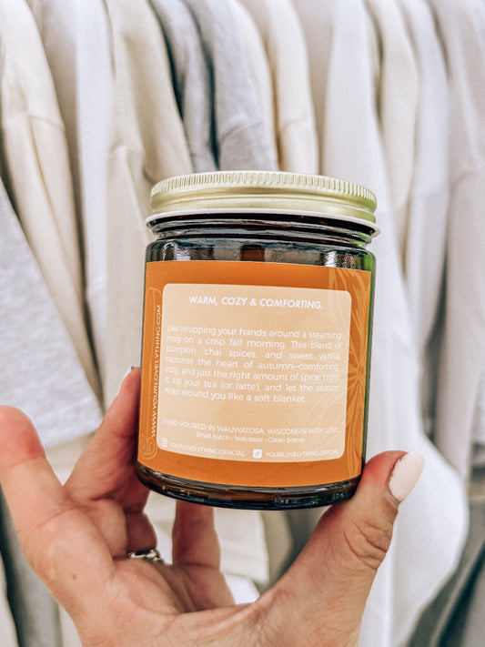 Hand holding a jar of candle with an orange label against a neutral background