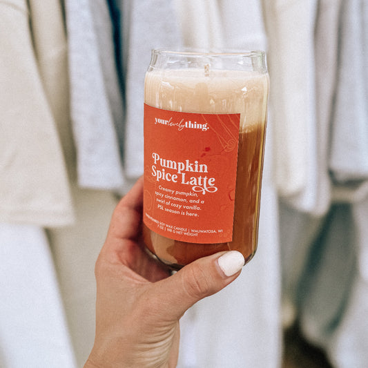 Candle labeled 'Pumpkin Spice Latte' held by a person with a neutral background