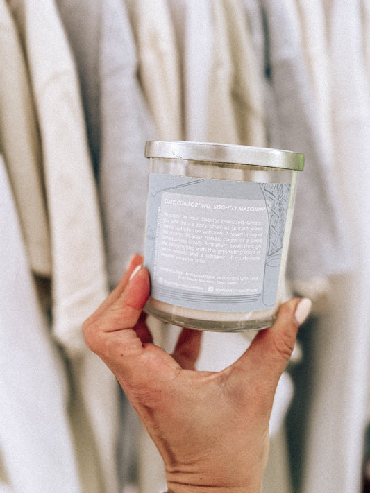 Hand holding a candle with a label against a neutral background