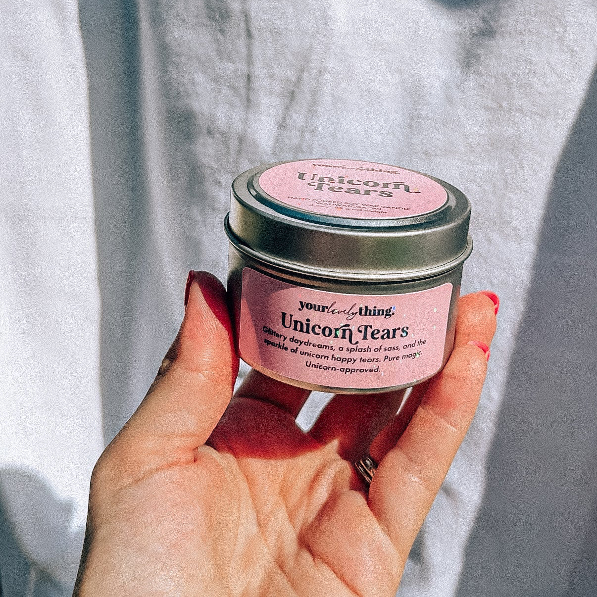 Hand holding a small pink jar with a silver lid against a light gray background