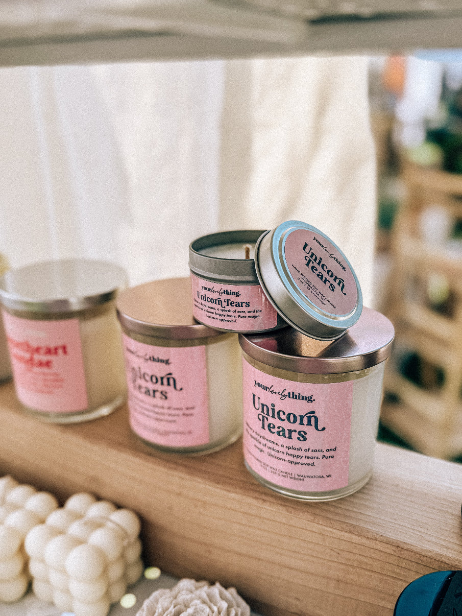 Candle jars with pink labels on a wooden shelf