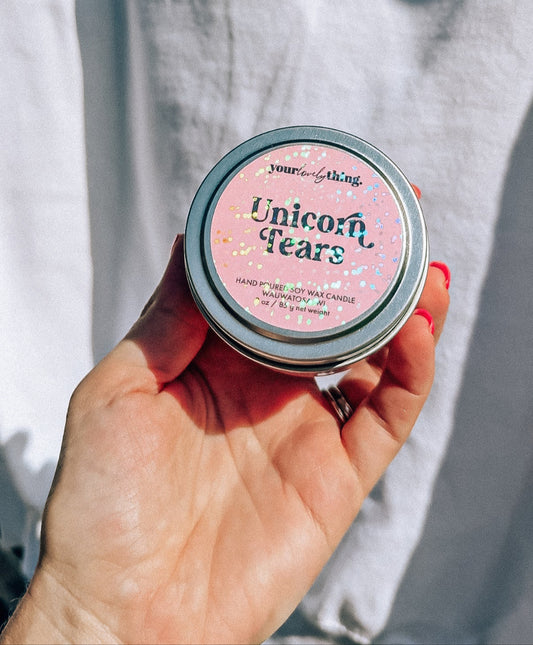 Hand holding a small round container labeled 'Unicorn Tears' against a light background