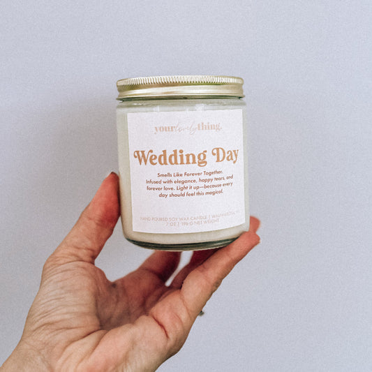 Hand holding a candle labeled 'Wedding Day' against a plain background