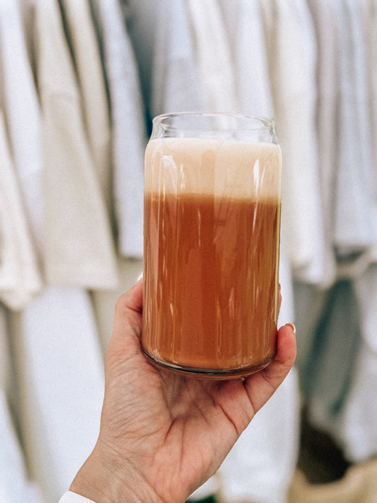 Hand holding a glass of layered coffee drink with a blurred background
