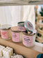 Candle jars with pink labels on a wooden shelf