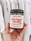 Hand holding a candle labeled 'Hot Apple Strudel' with a neutral background